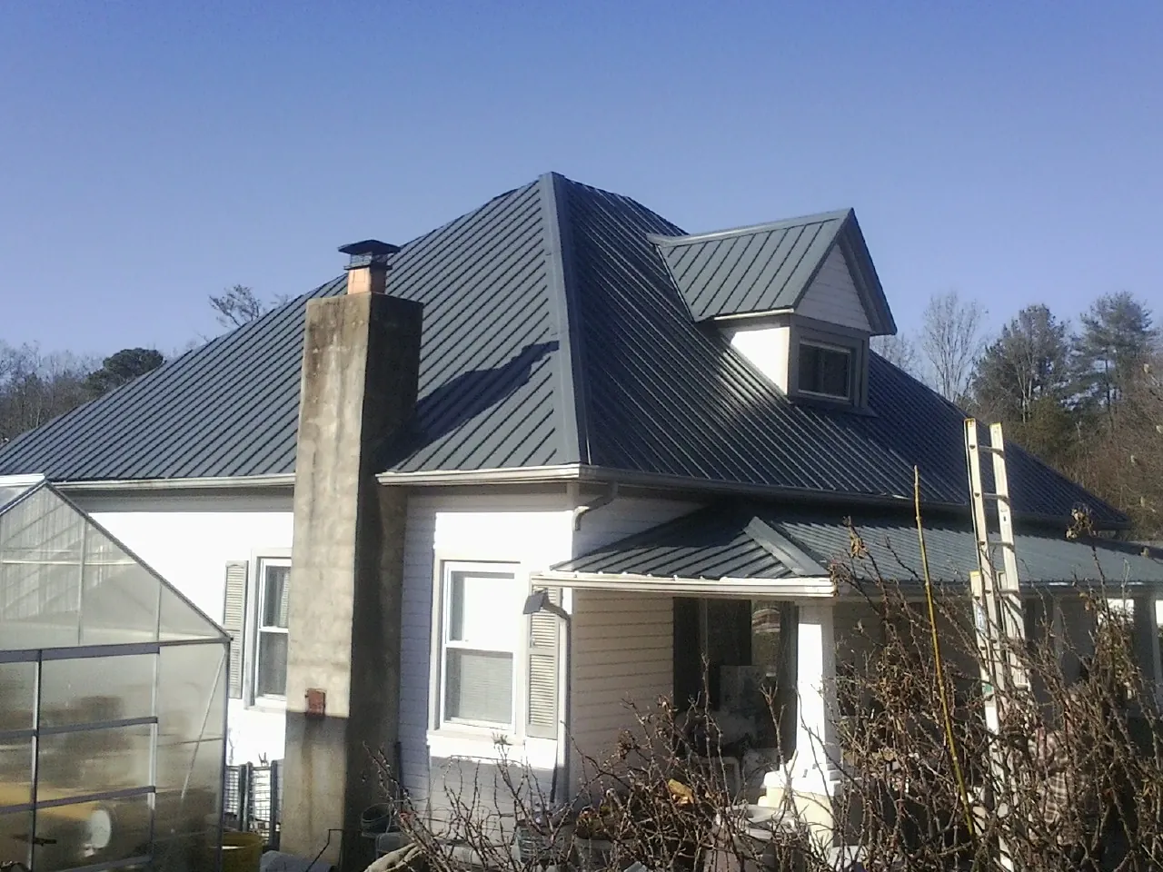 Dark blue standing seam metal roof on a white farmhouse with dormer — Slate & Tile Roof Repair by Roofing Brothers in Whitleyville