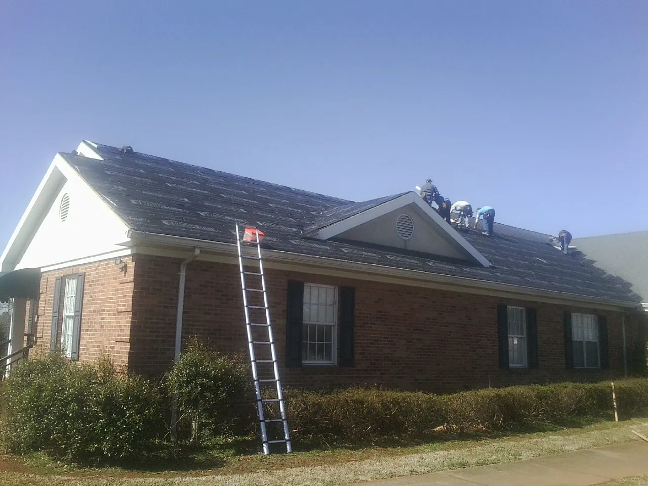 Crew tearing shingles off a brick ranch roof with a ladder set — Emergency Roof Repair work by our crew in Whitleyville