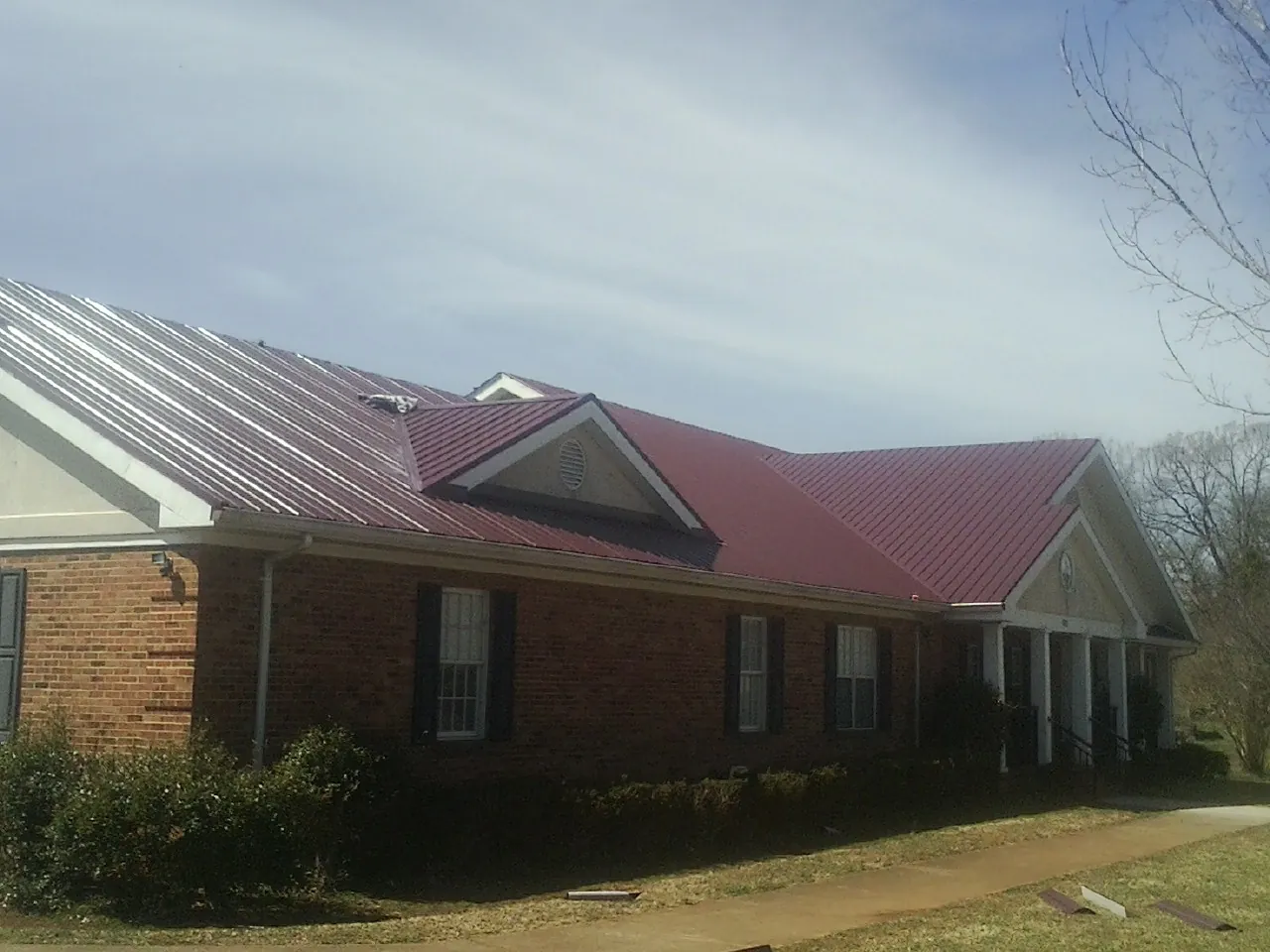 Red metal roof with gabled entries on a long brick building, from a Hail Damage Roof Repair job in Whitleyville