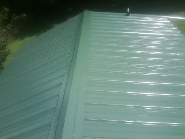 New green metal panels meeting at the ridge of a roof — Flat Roof Repair work by our crew in Whitleyville