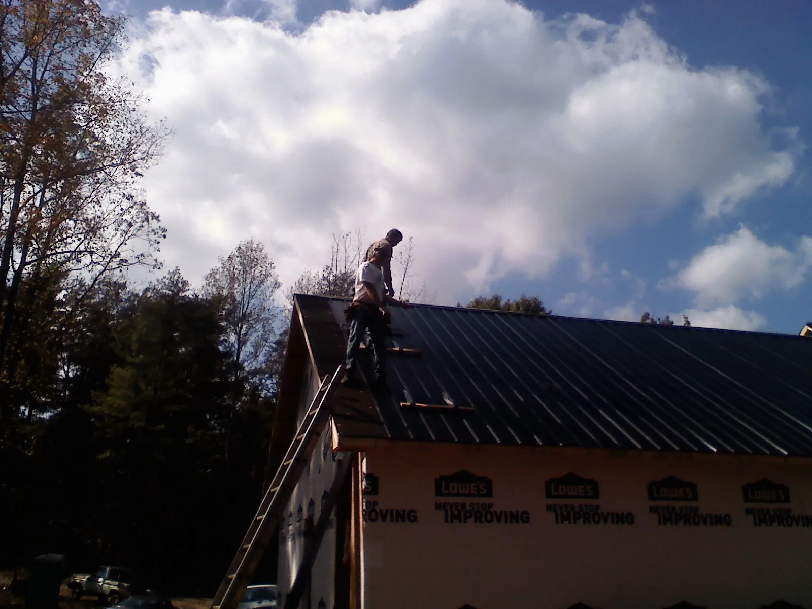 Roofer fastening dark metal panels high against a cloudy sky, from a Roof Inspection job in Whitleyville