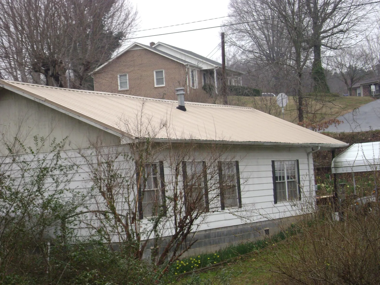 Tan metal roof on a white sided house set into a hillside — Commercial Roofing by Roofing Brothers in Whitleyville