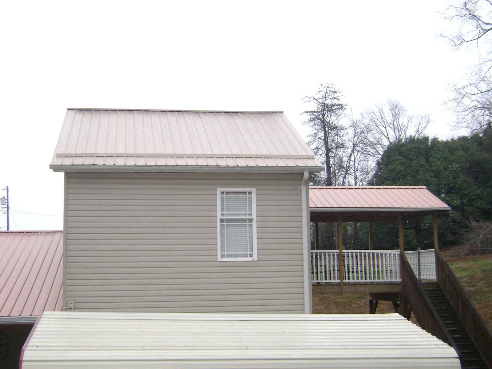 Tan metal roofs on a two story addition and attached porch, from a Roof Replacement job in Whitleyville